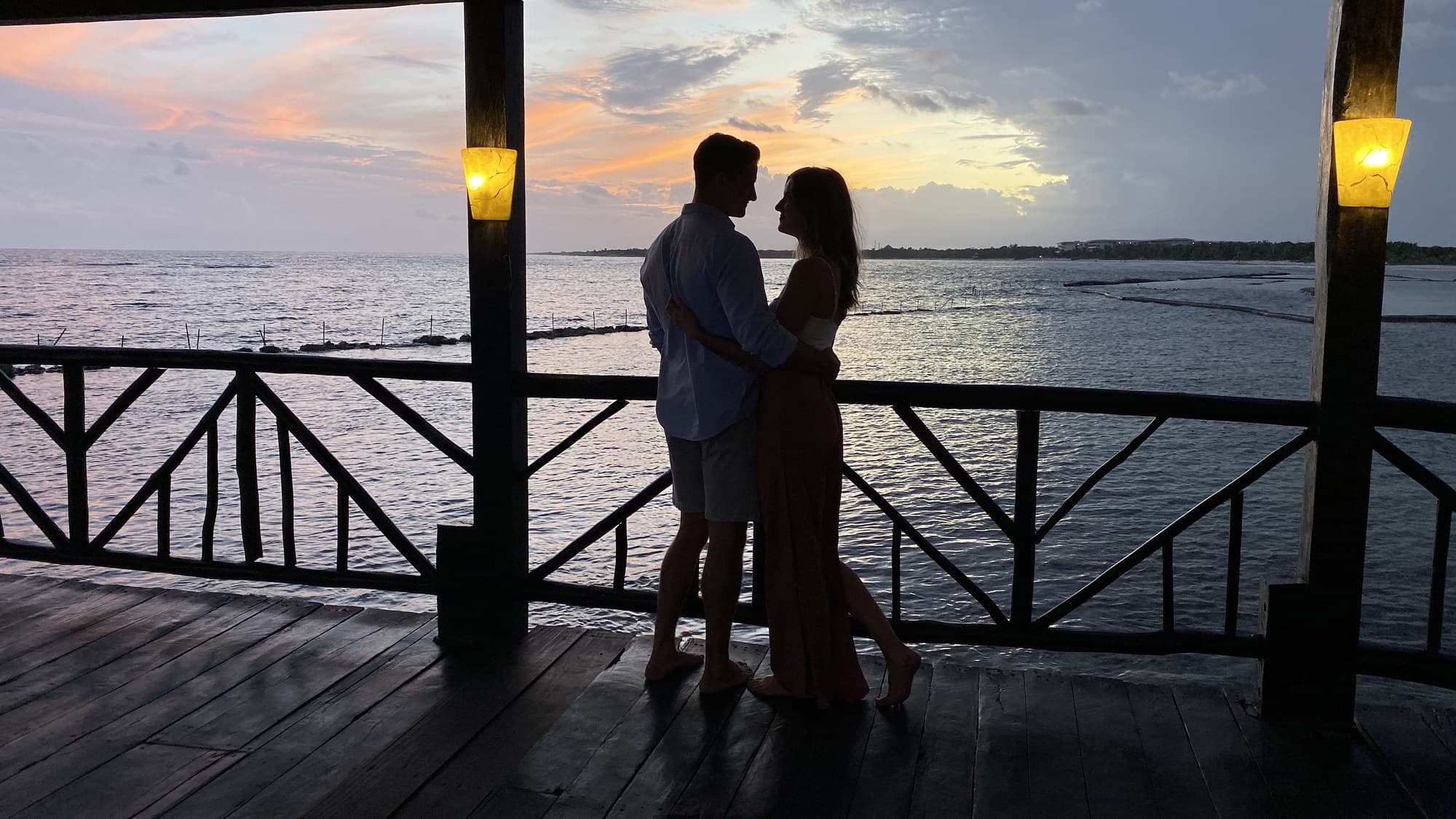 Couple embracing on a wooden balcony at sunset over the water